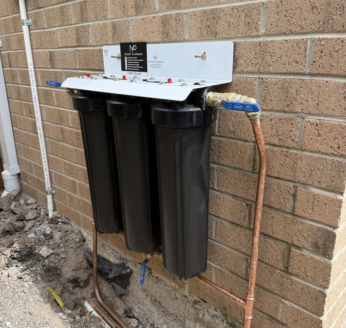 Three-stage whole-house water filtration system mounted on a brick wall
