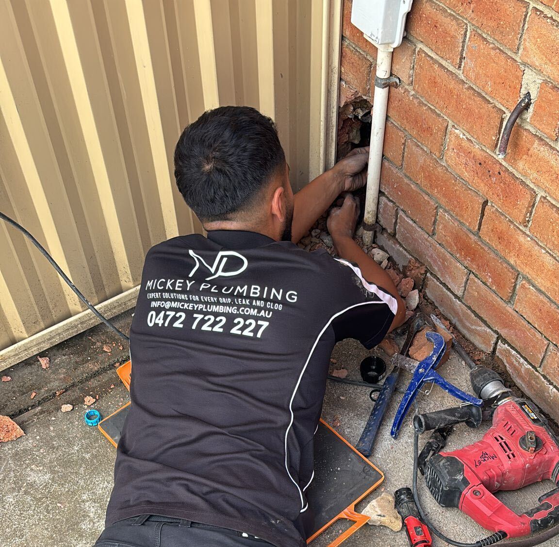 Murat from Mickey Plumbing working on pipework at a brick wall